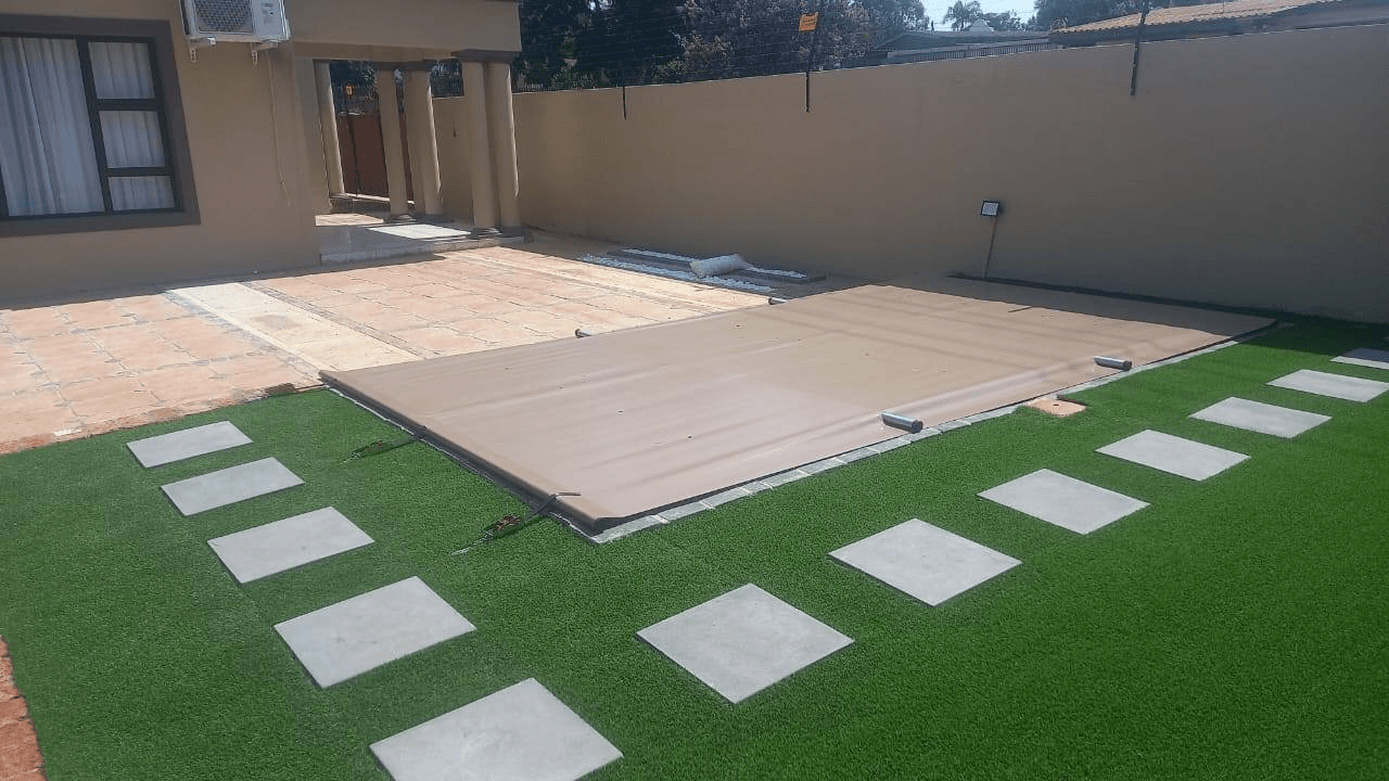 Beige PVC pool cover installation with landscaped garden and stepping stones