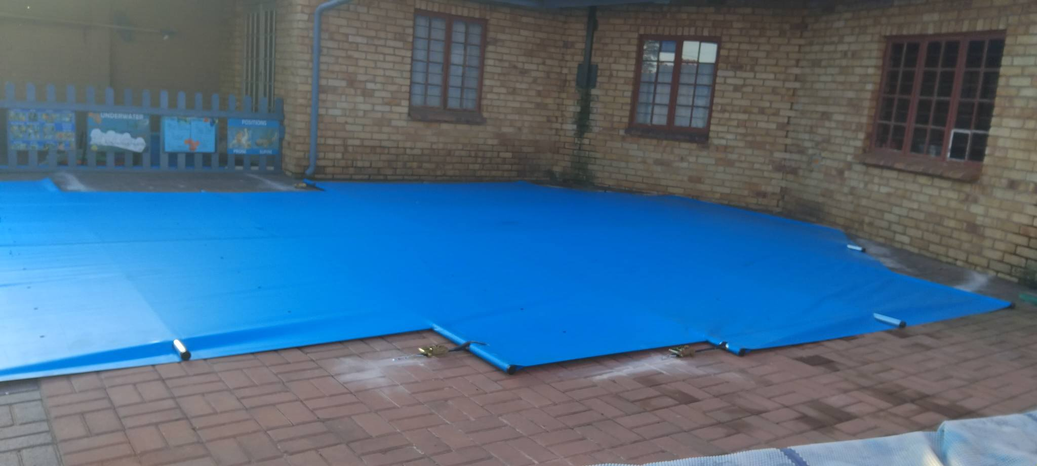 Blue PVC pool cover installed on brick paving with tropical garden backdrop